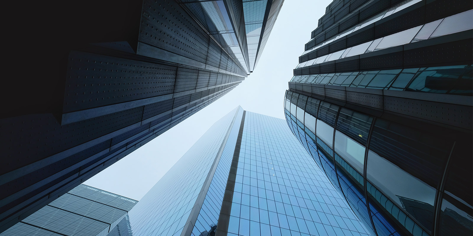 Low-angle view of modern glass skyscrapers reflecting surrounding buildings and blue sky.