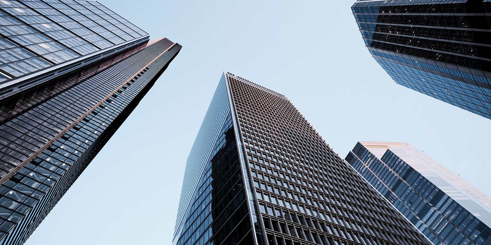 Low-angle view of modern skyscrapers with reflective glass facades against a clear sky.