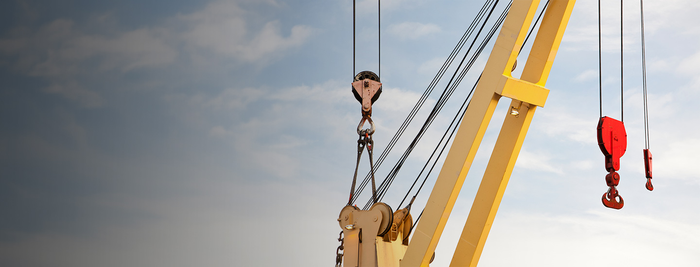Top section of a yellow construction crane with pulleys and cables against a cloudy sky.