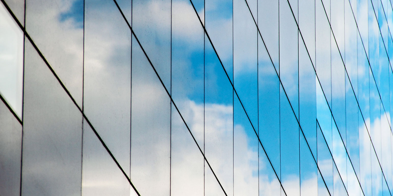 Reflection of a cloudy sky on grid-patterned glass windows of a modern building.