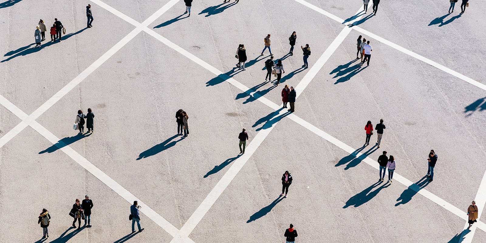 Aerial view of people scattered across a grid-marked open space with long shadows.