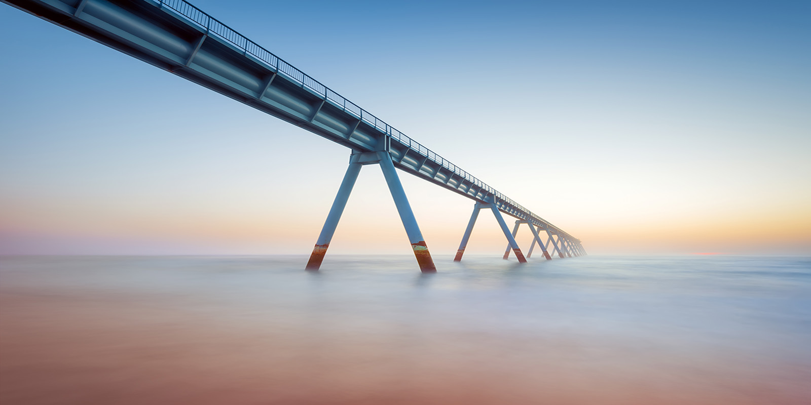 Long pier with railings and support beams extending over calm sea.