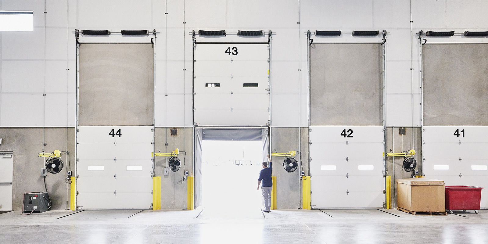Warehouse loading area with garage doors numbered 41 to 44 and a person waiting at the open centre door.