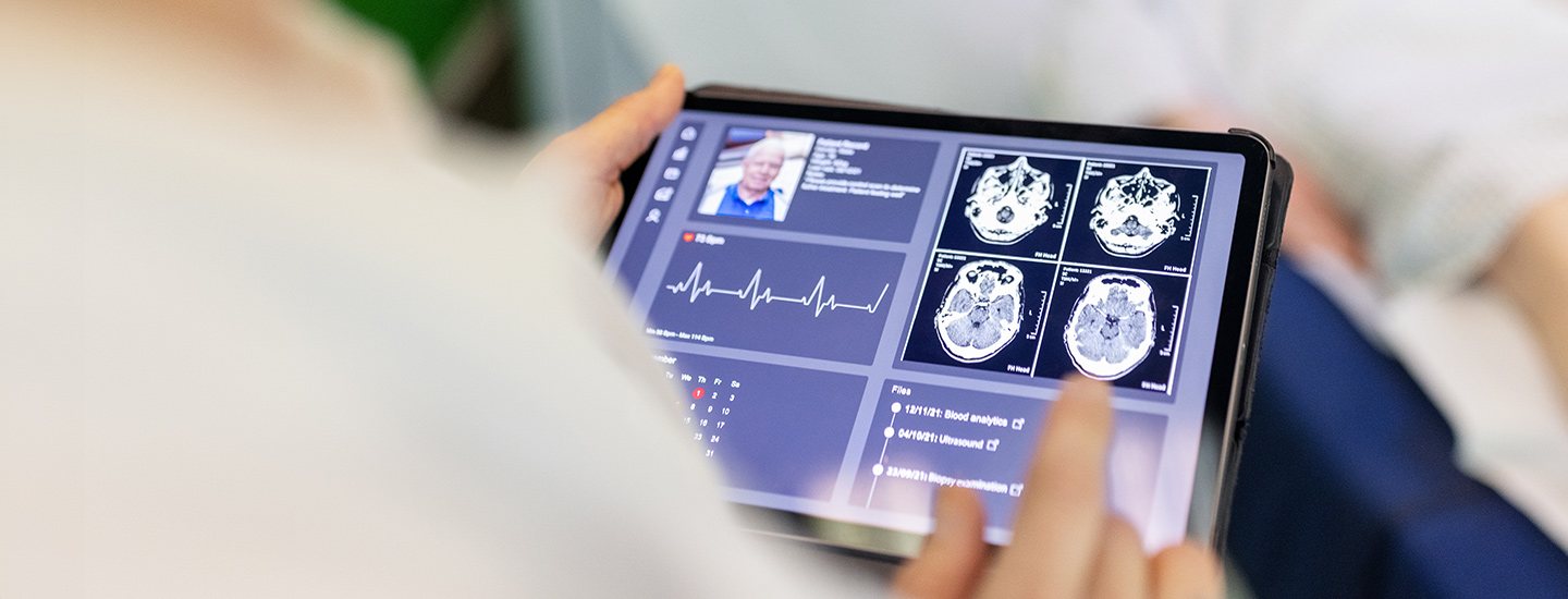 Person holding a tablet showing medical data including brain scans, ECG graph, and a profile image of an elderly man.