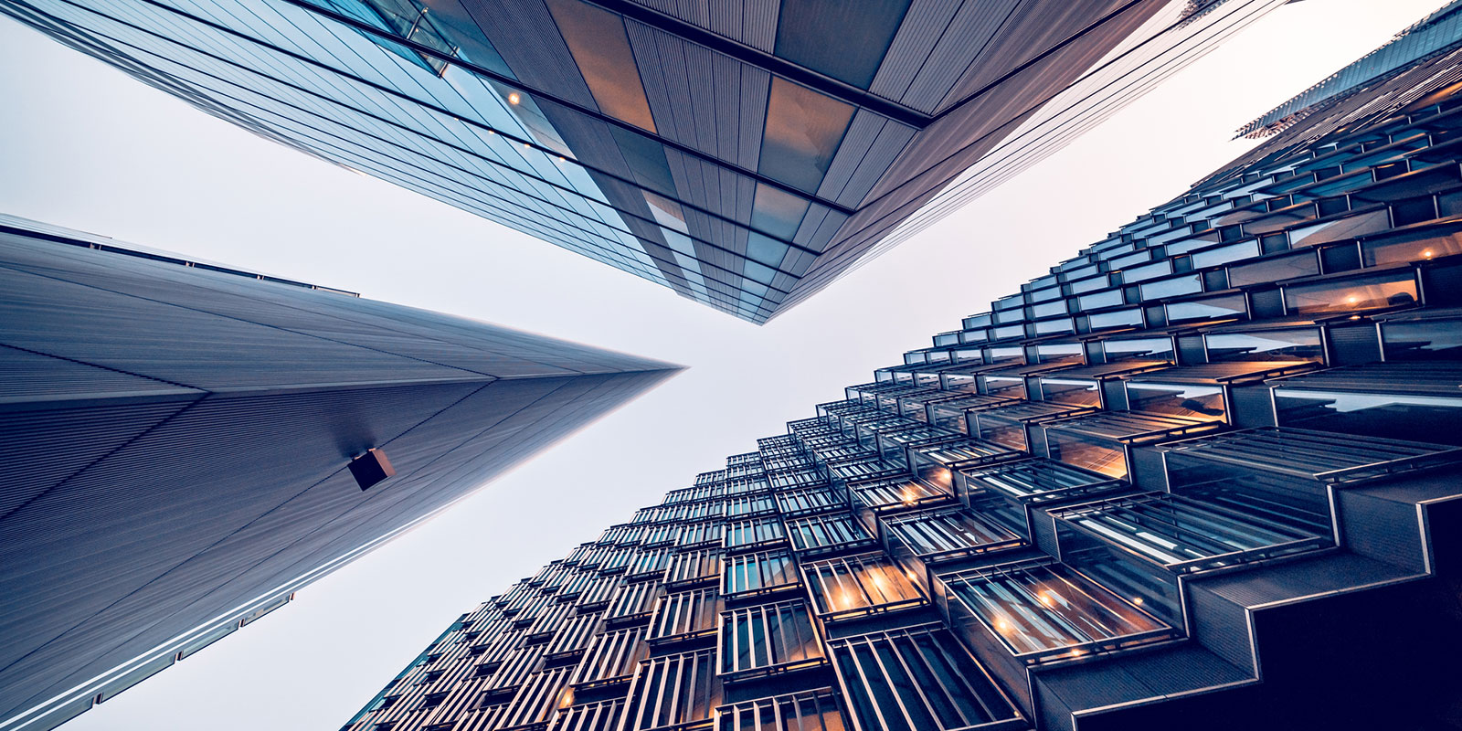 Upward view of three modern high-rise buildings with glass and metal facades, converging towards the sky.