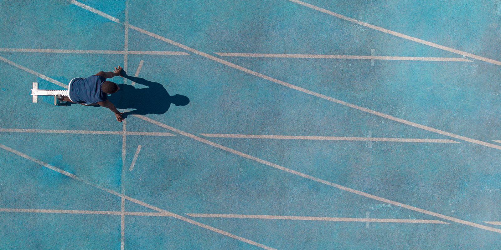 Overhead view of a person at the starting blocks on a blue running track with white lane markings.