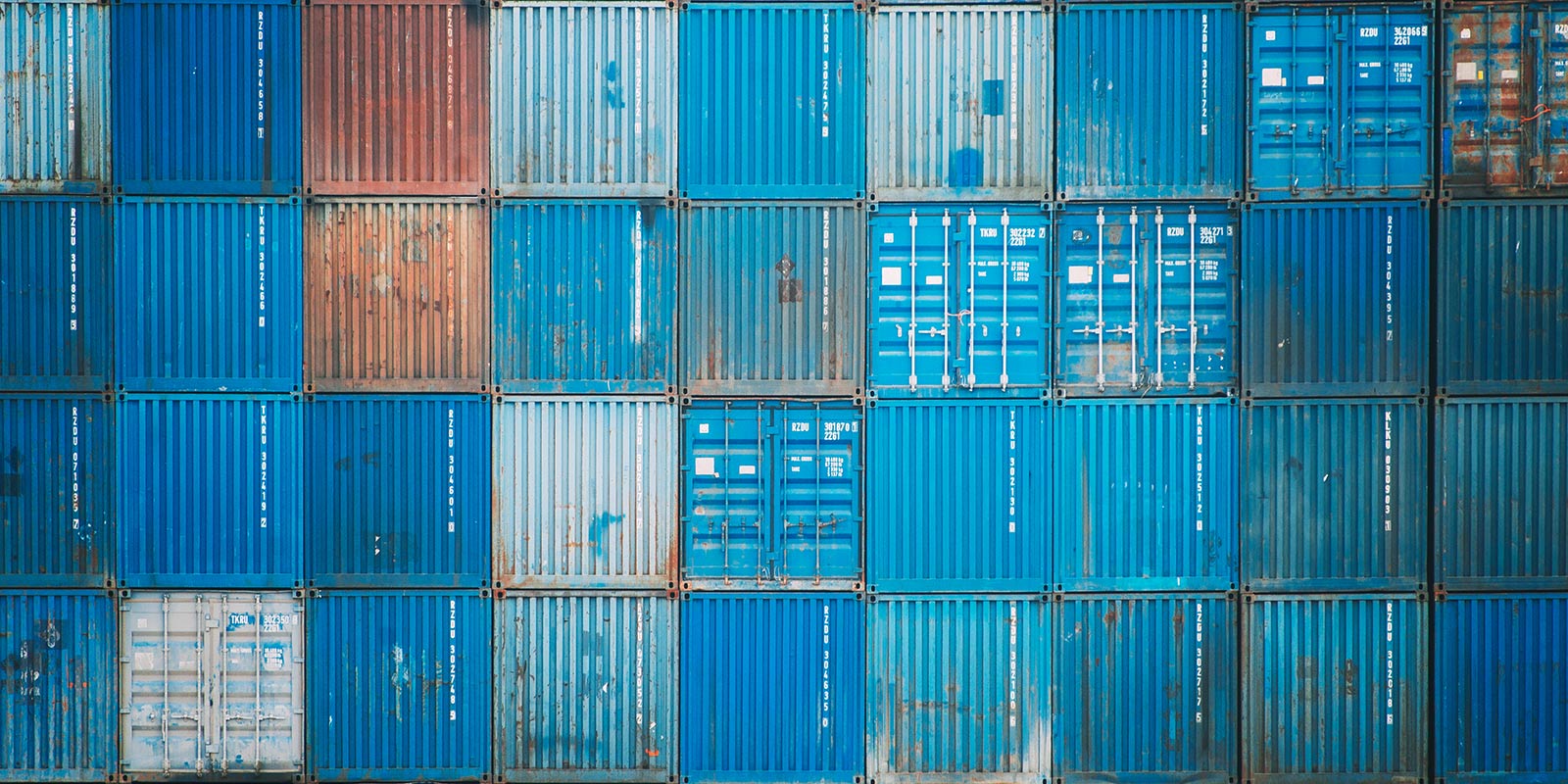 Stack of blue shipping containers, with some showing rust and wear.