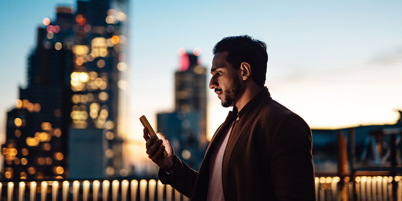 Person holding a smartphone, with a city skyline in the background.