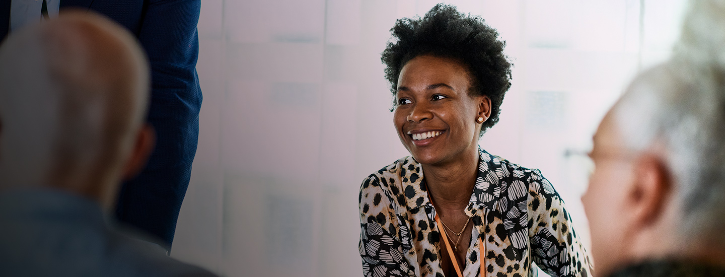 Group of people in discussion indoors, with a person in a patterned shirt at the centre.