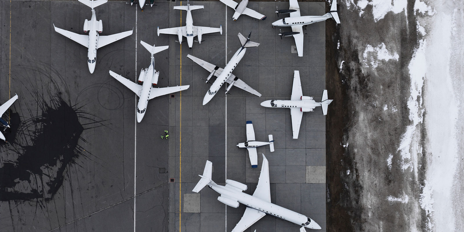 Aerial view of airport tarmac with parked planes, white markings, and snow-covered ground.