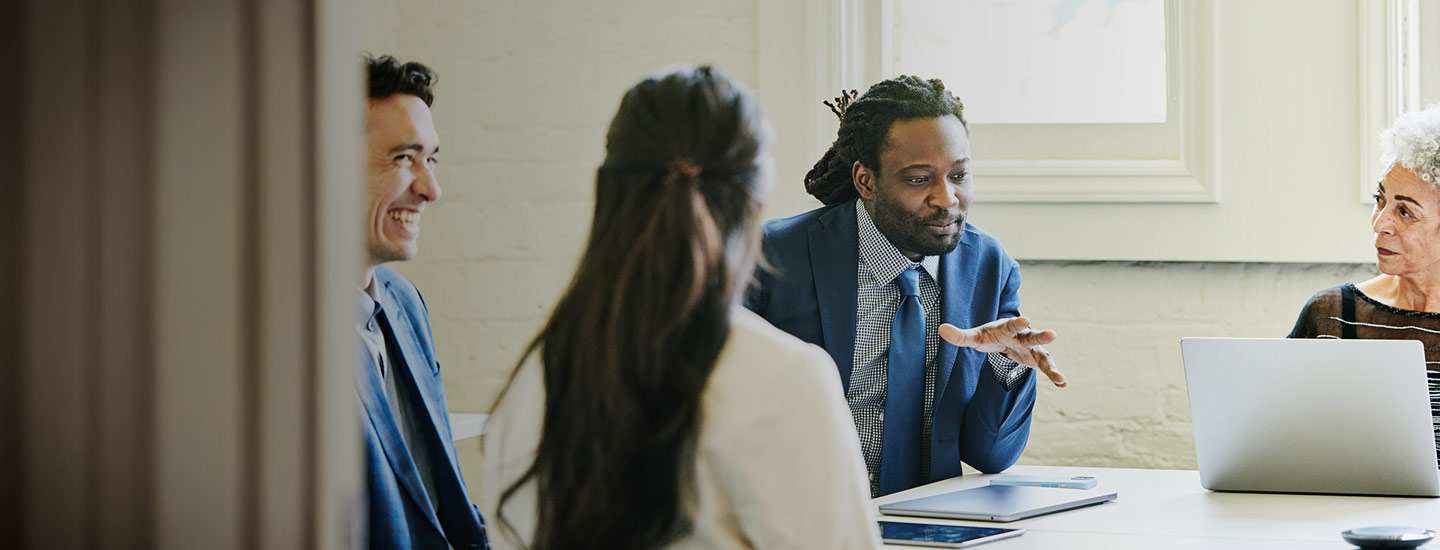 Four people seated around a table in discussion, with a laptop and tablet visible.