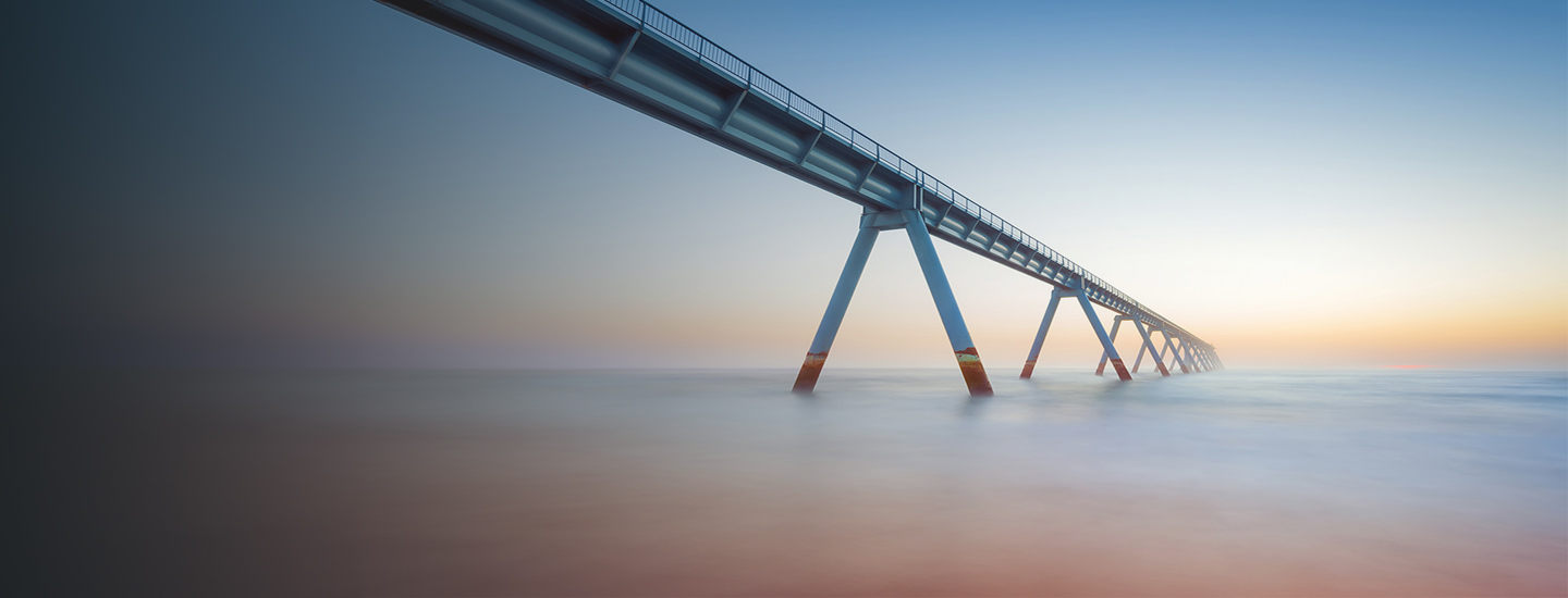 Elevated pipeline or bridge over calm water at sunrise or sunset.
