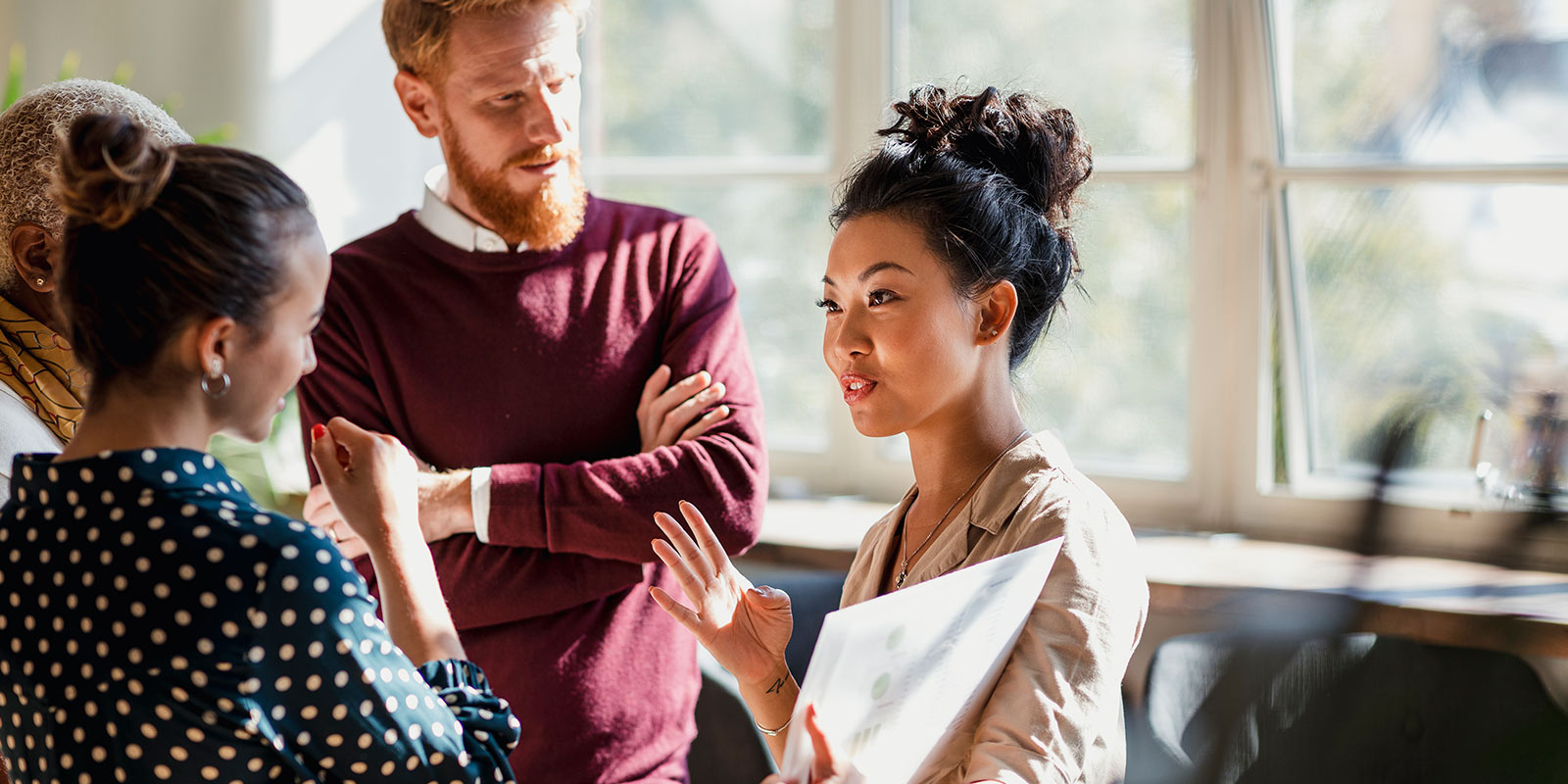 Four people standing indoors having a discussion, with one holding a folder.