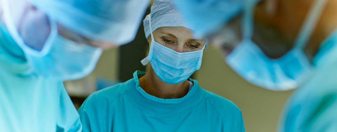 Three individuals in surgical attire, including masks and caps, in a medical setting.