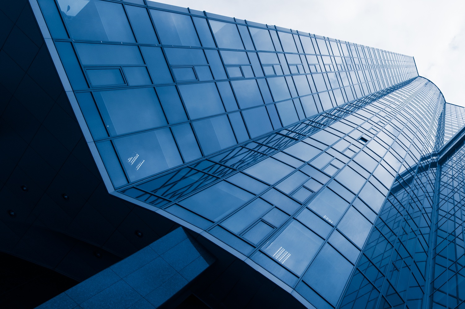 Multi-level modern building with curved walkways, large geometric glass windows, and an urban landscape with water visible outside.