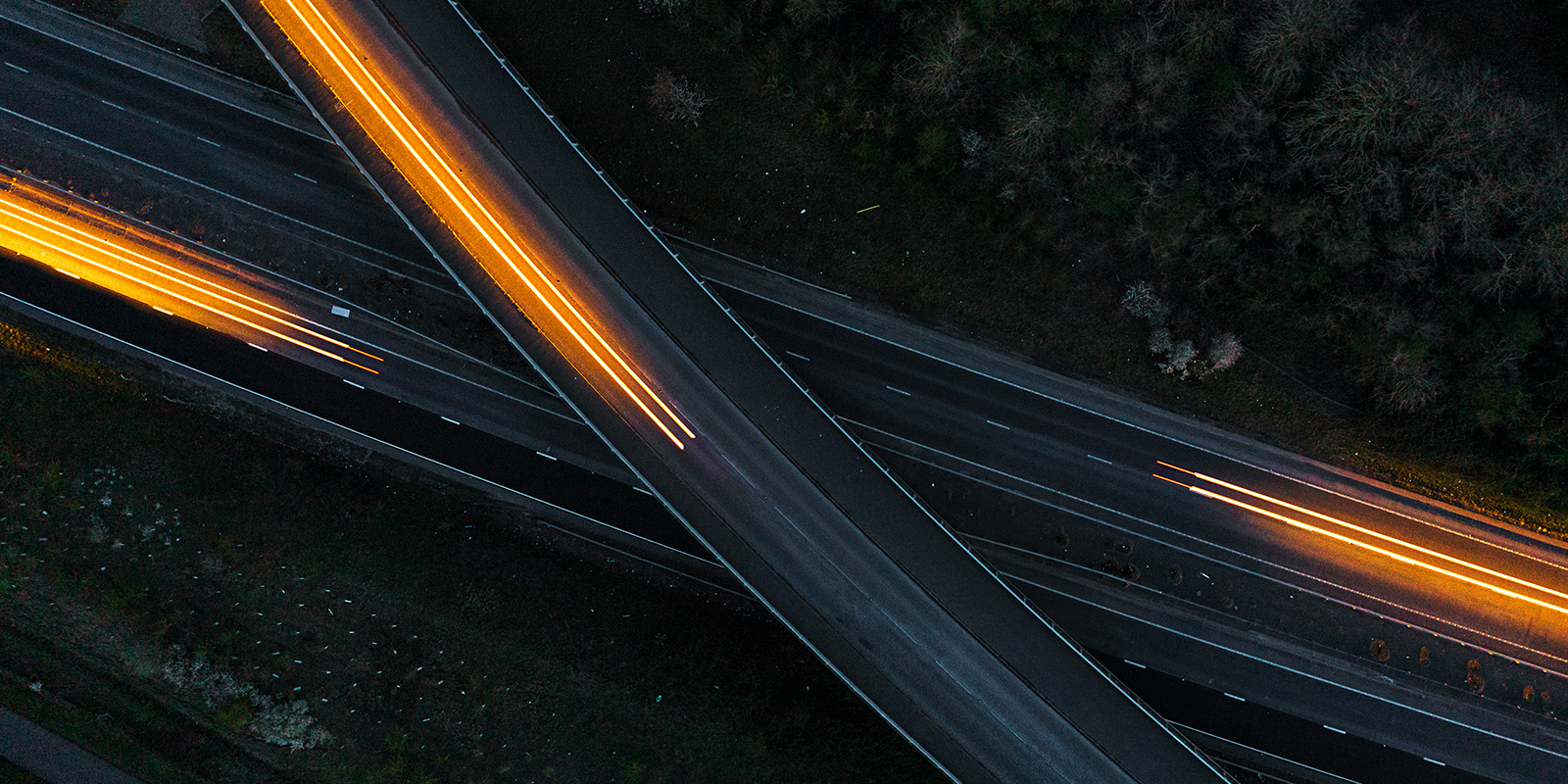 Aerial view of illuminated motorway junction at night with light streaks from vehicles.