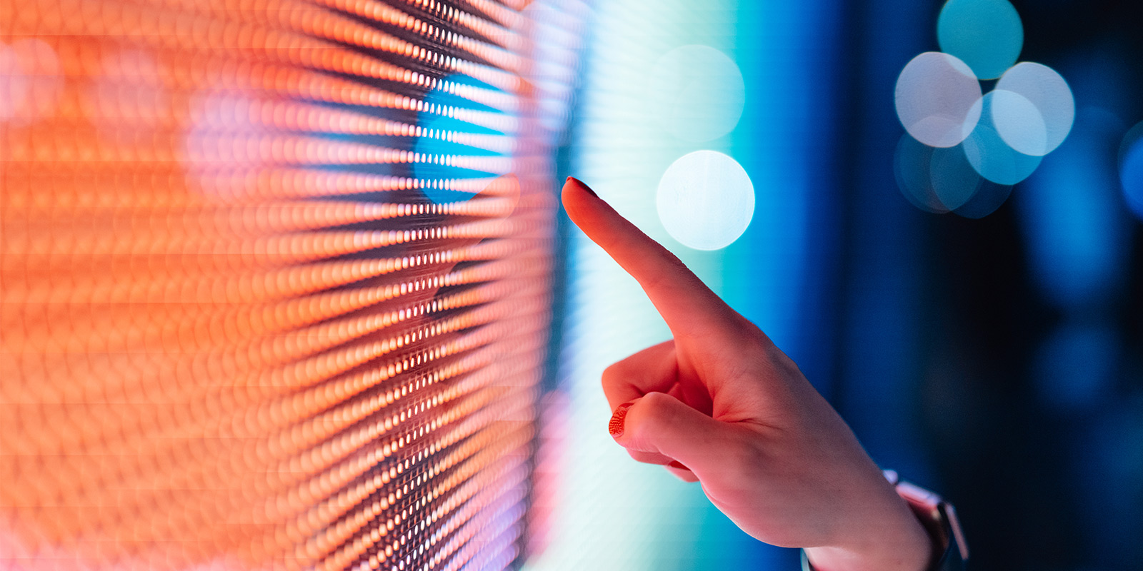 Close-up of a hand pointing at a colourful LED screen with vibrant orange and blue lights.