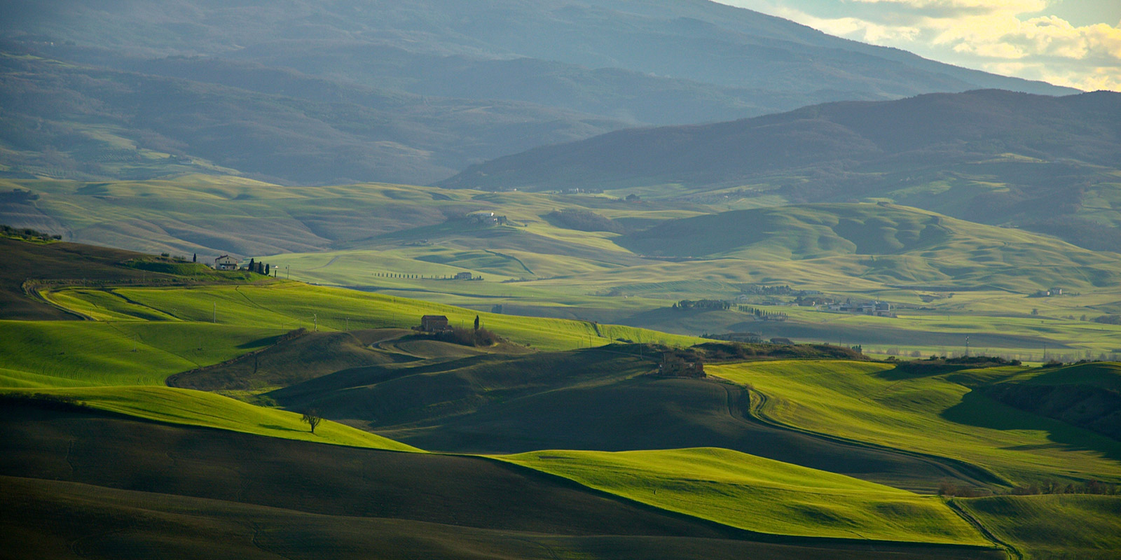 Scenic view of rolling green hills, scattered buildings, and partly cloudy sky.