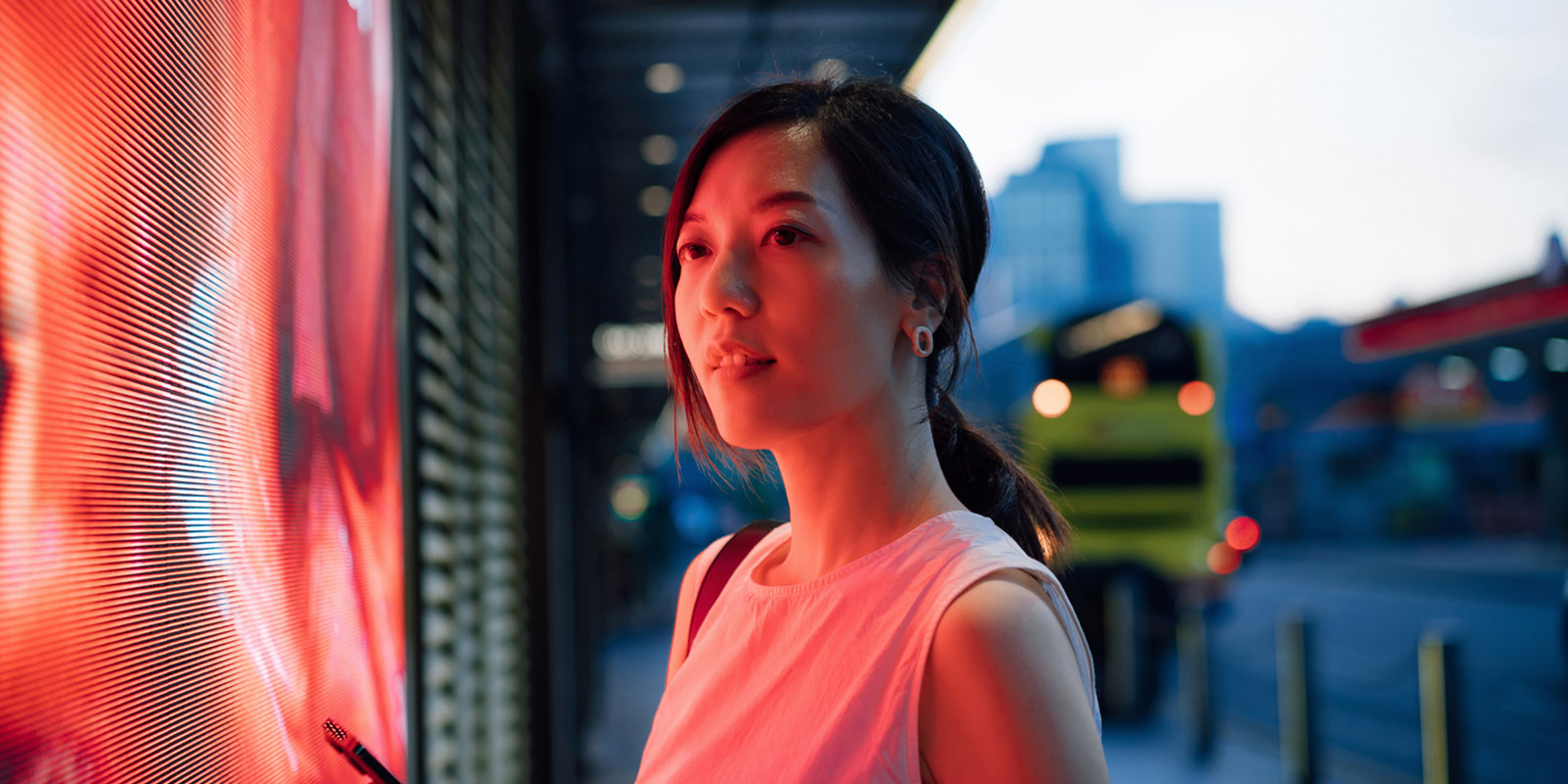 Person standing in front of a bright display screen with a yellow bus and buildings in the background.