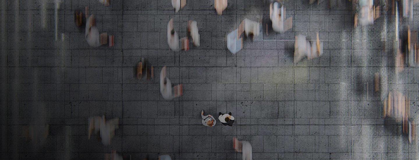 Top-down view of a tiled floor with blurred figures walking; two people stand still in the centre.