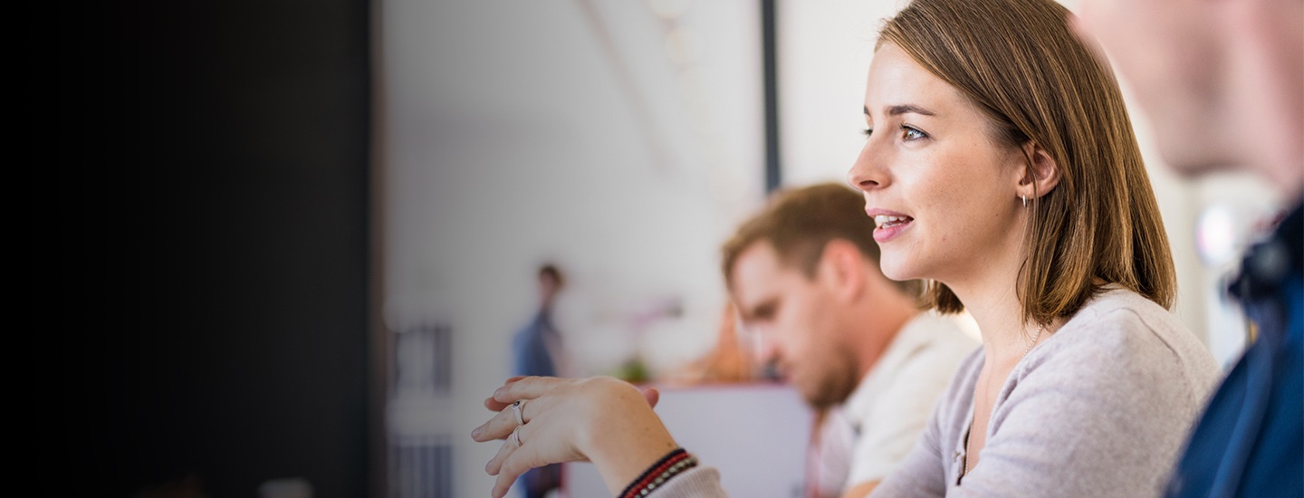Group of people seated in discussion, with one person in focus; others and background slightly blurred.