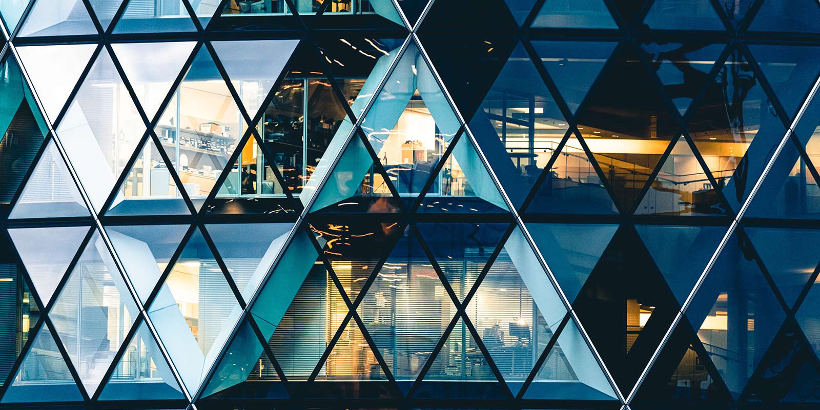 Exterior of a modern building with triangular glass panels, showing lit office spaces inside.