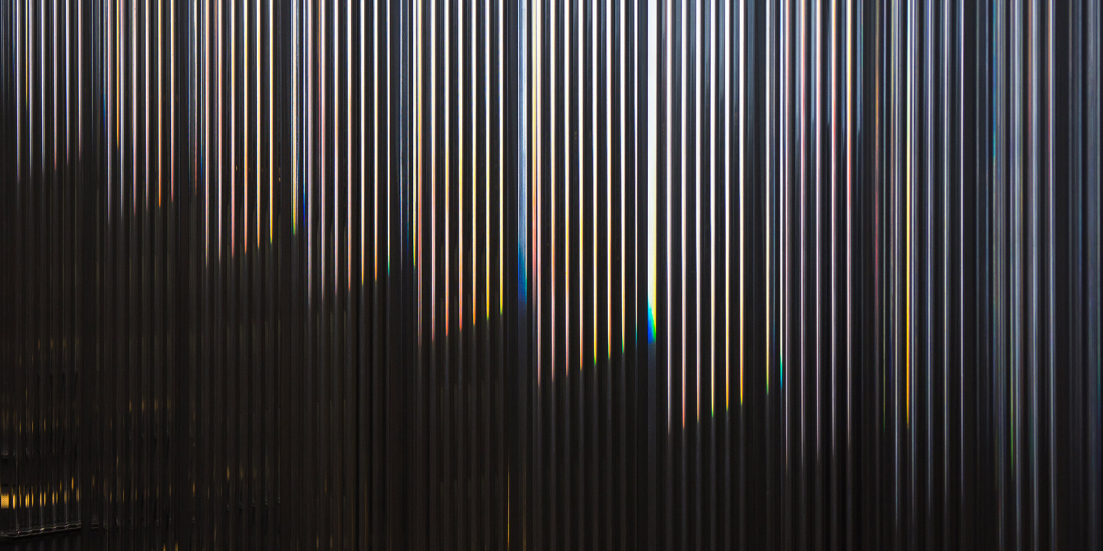 Close-up of a corrugated metal surface with vertical ridges and subtle rainbow-like reflections.