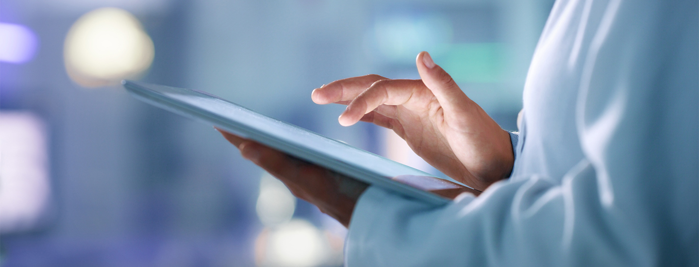 Close-up of a medical professional in a white lab coat using a tablet indoors, with a blurred background.