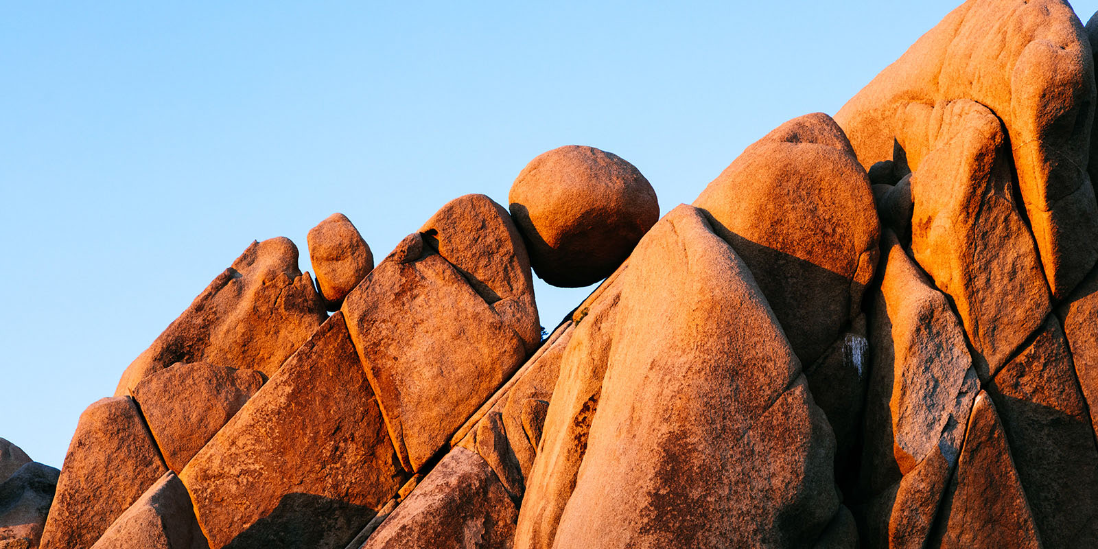 Natural rock formation with a spherical reddish-brown boulder balanced atop other rocks under a clear blue sky.