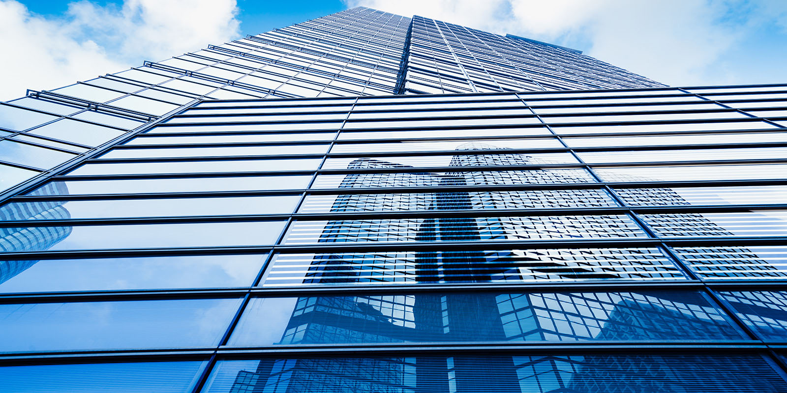 Low-angle view of a modern skyscraper with reflective glass windows showing building reflections.