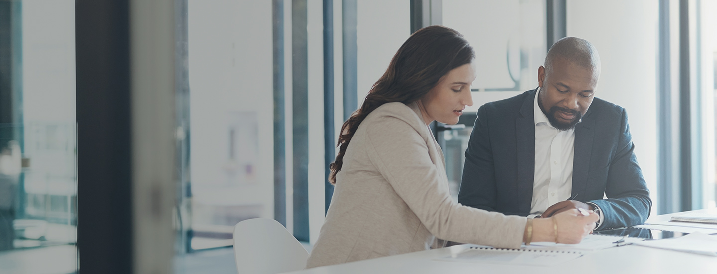 Two people seated at a table in an office, discussing a document.