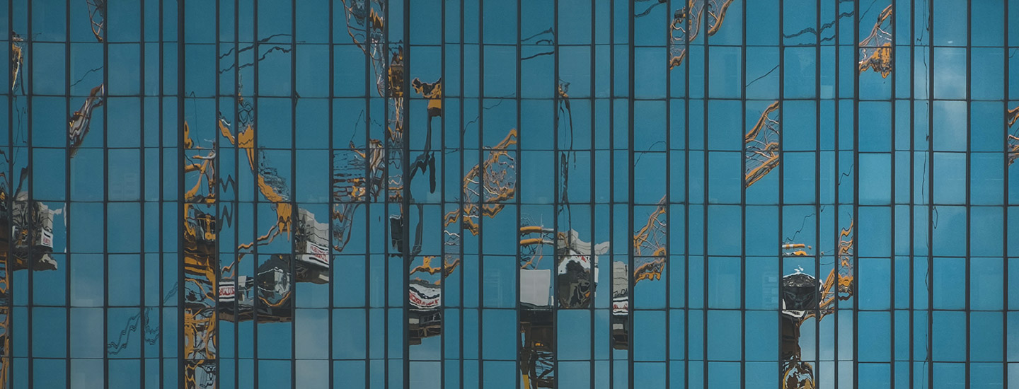 Distorted reflections of cranes on a blue glass building facade, forming abstract patterns.