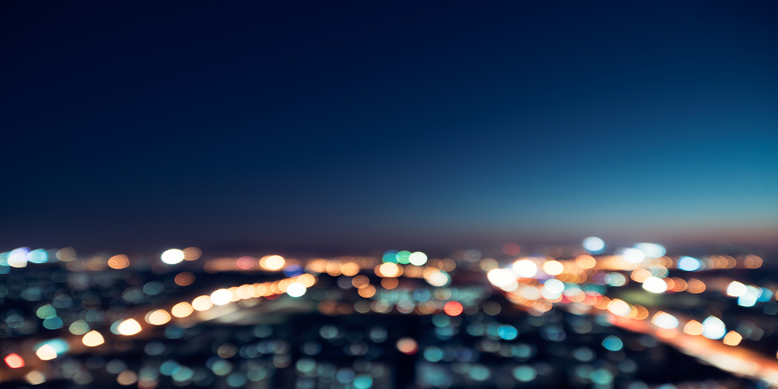 Blurred cityscape at night with bokeh lights and a dark blue sky.
