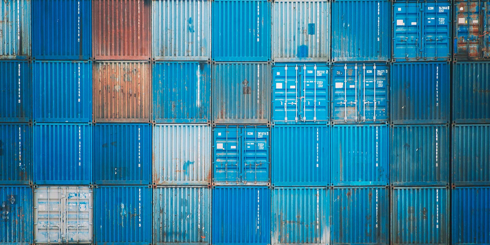 Stacked shipping containers with varied shades and signs of weathering.