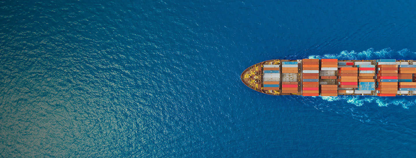 Aerial view of cargo ship loaded with colourful containers sailing through deep blue ocean.