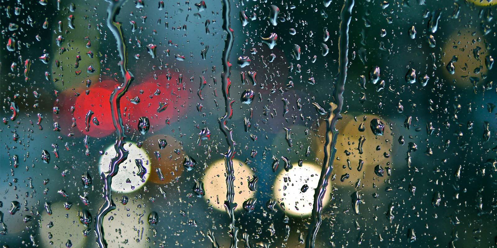Rain-covered window with blurred street and vehicle lights creating a bokeh effect.