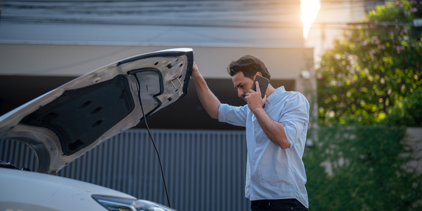 Person beside car with open bonnet, holding it up and talking on mobile.