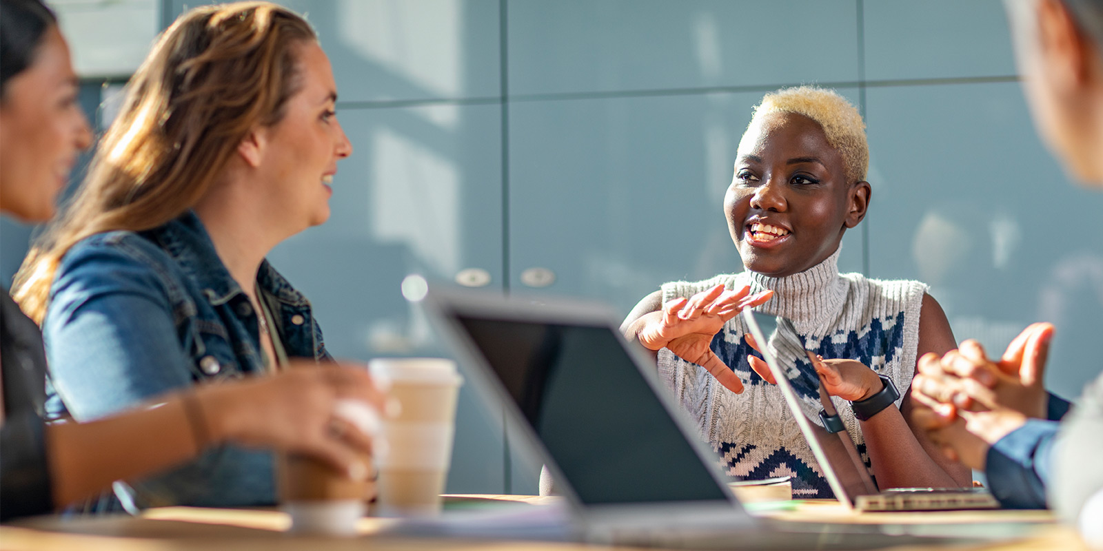 Group of people in a meeting room, seated around a table with laptops and coffee cups.