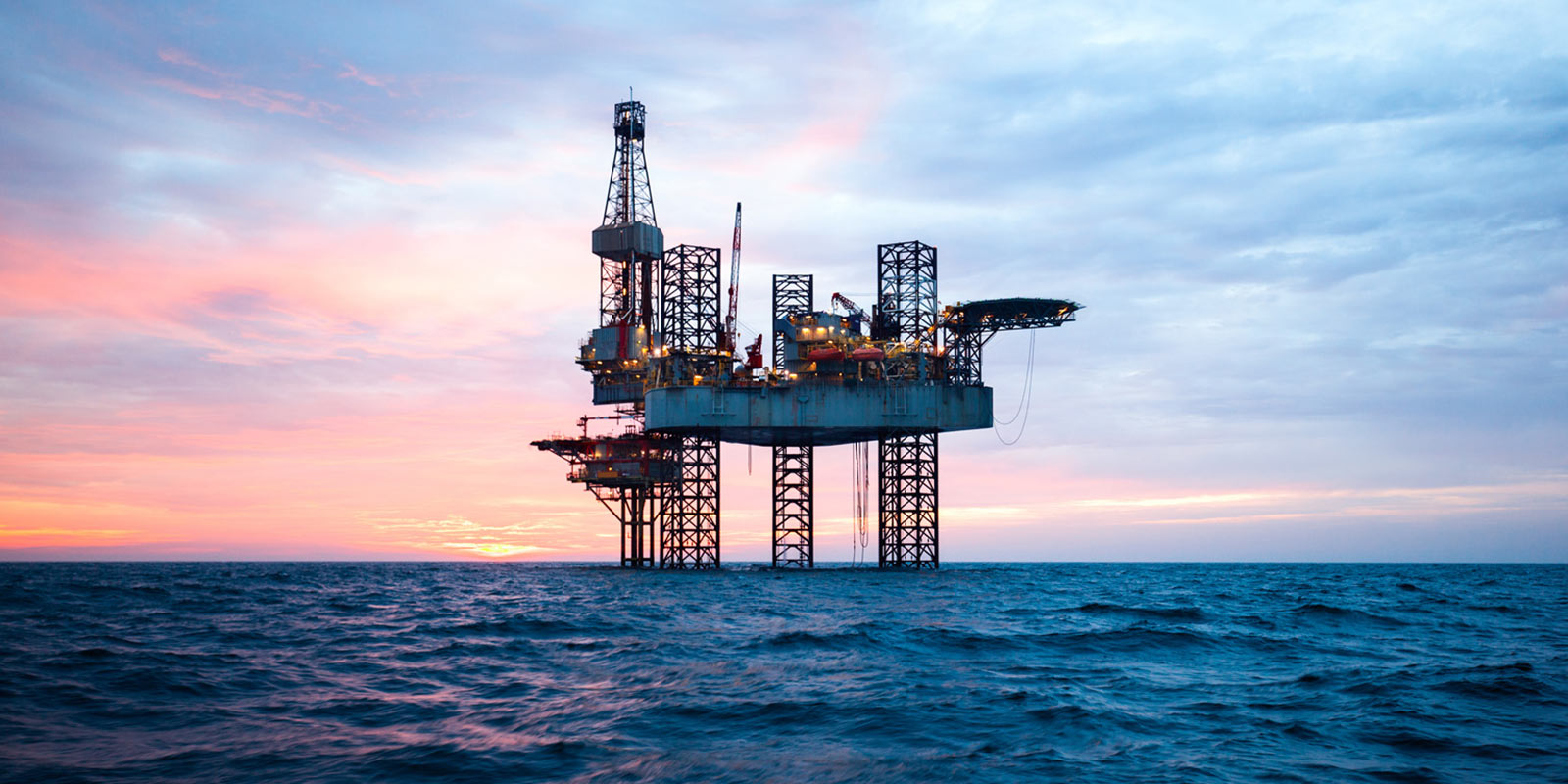 Offshore oil rig platform at sunset, with pink, orange, and blue hues in the sky.