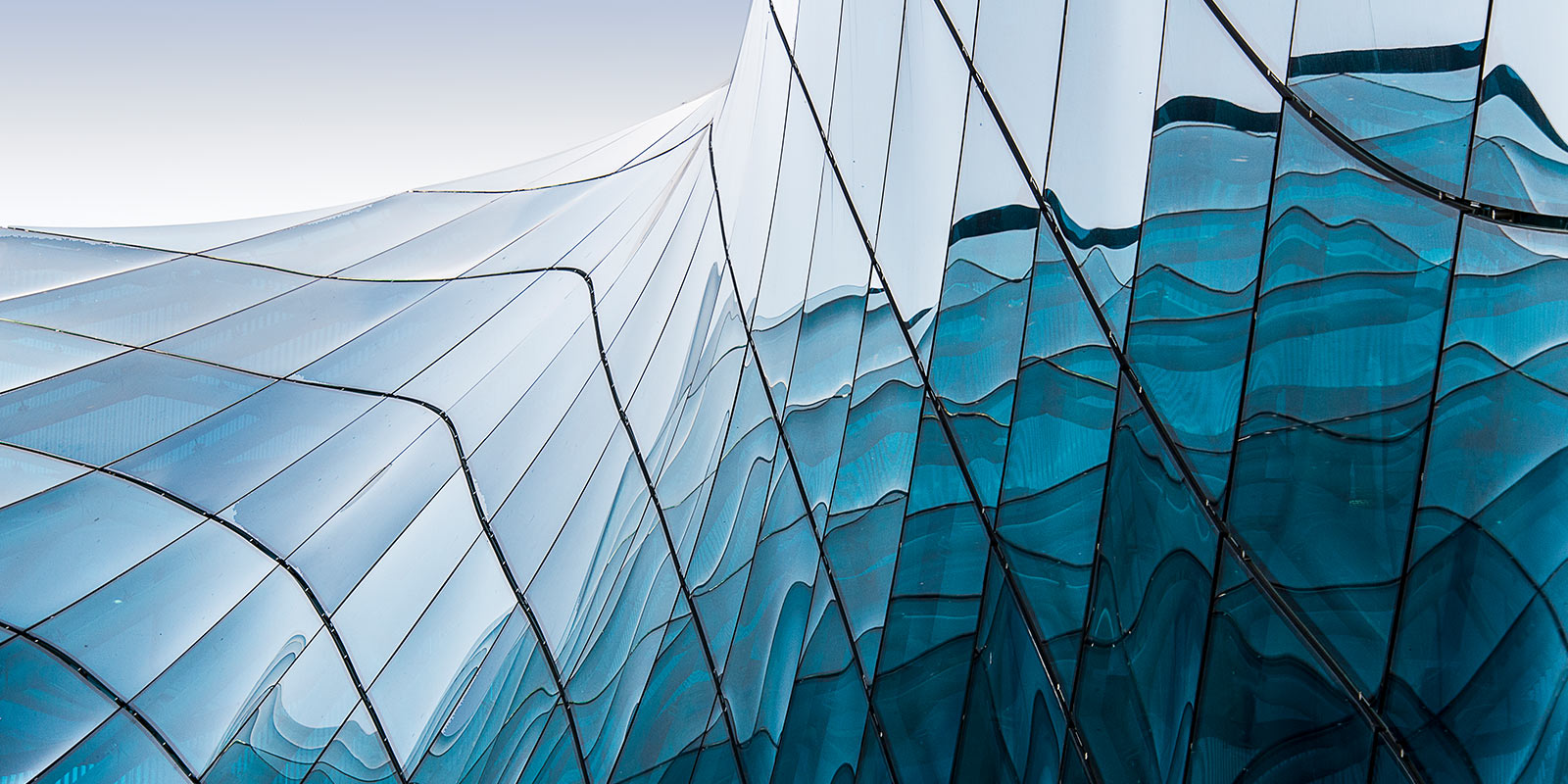 Modern building with a wavy glass facade reflecting the sky.