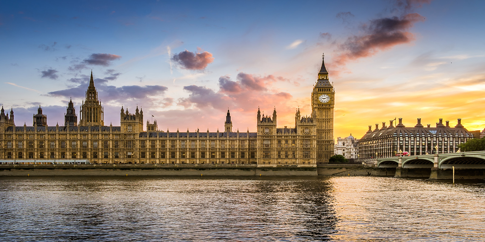Palace of Westminster and Big Ben at sunset, with vibrant sky colours reflected on the River Thames in the foreground.
