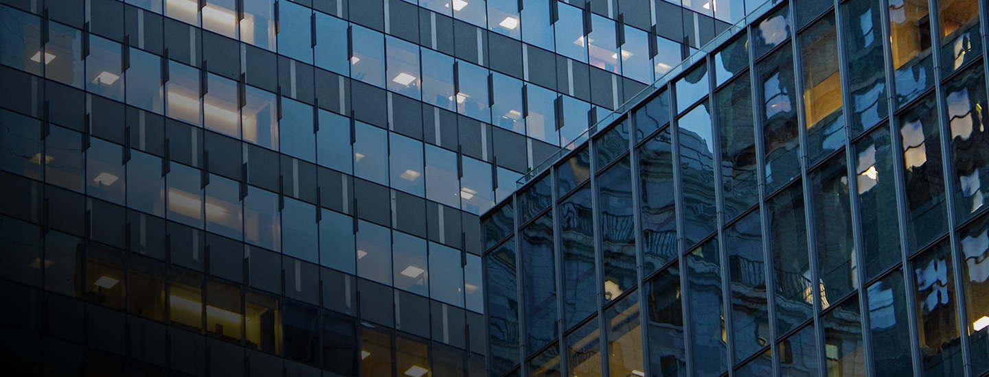Modern office building with reflective windows showing surrounding buildings and sky.