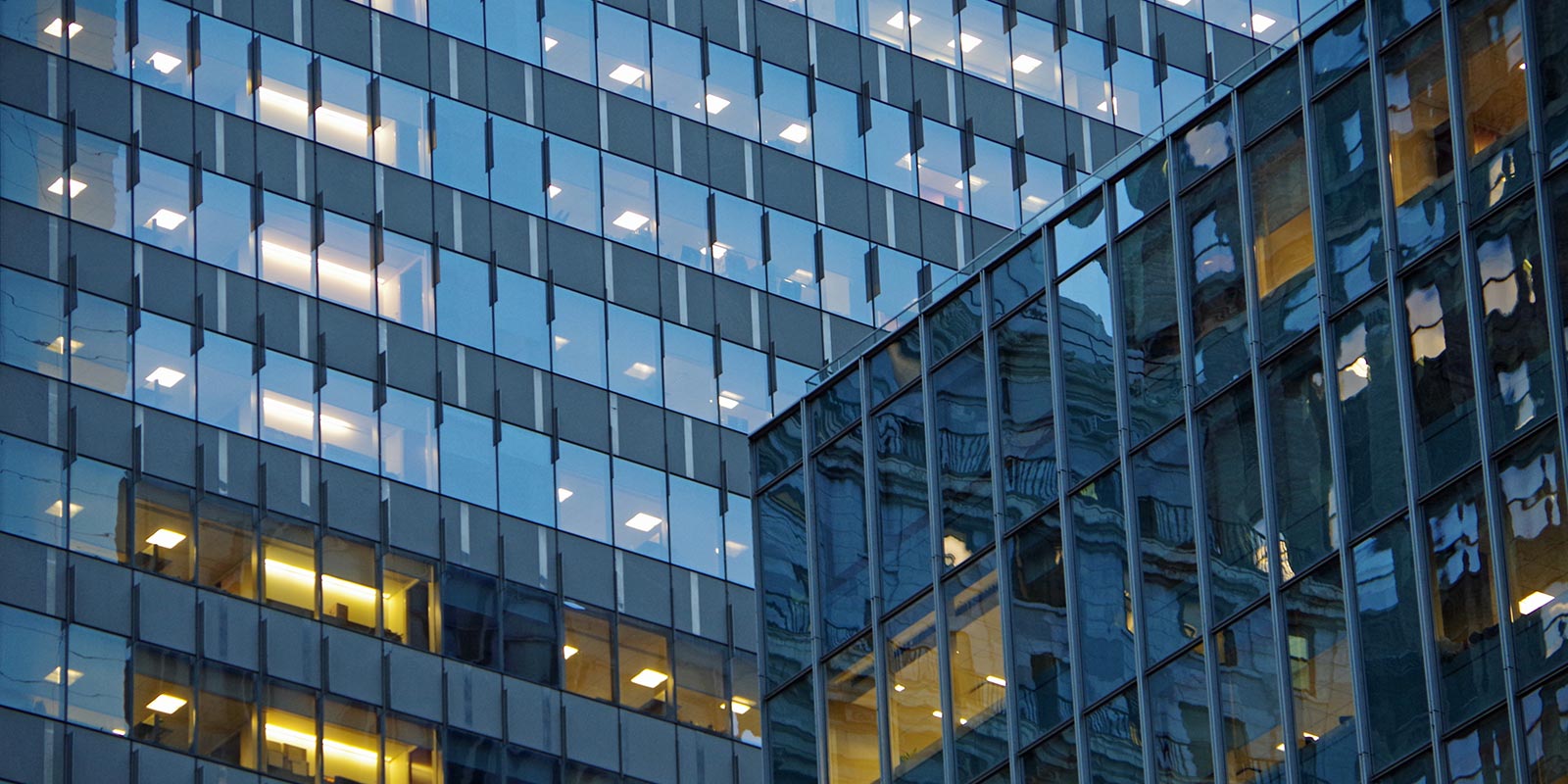 Exterior of a modern glass office building with reflections and illuminated windows.