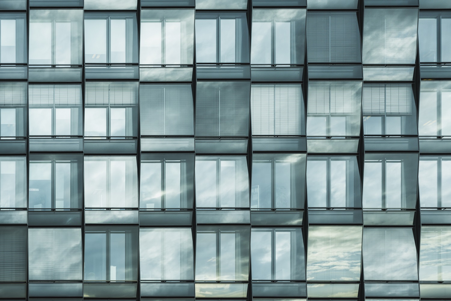Modern building facade with grid-patterned windows reflecting sky and clouds.