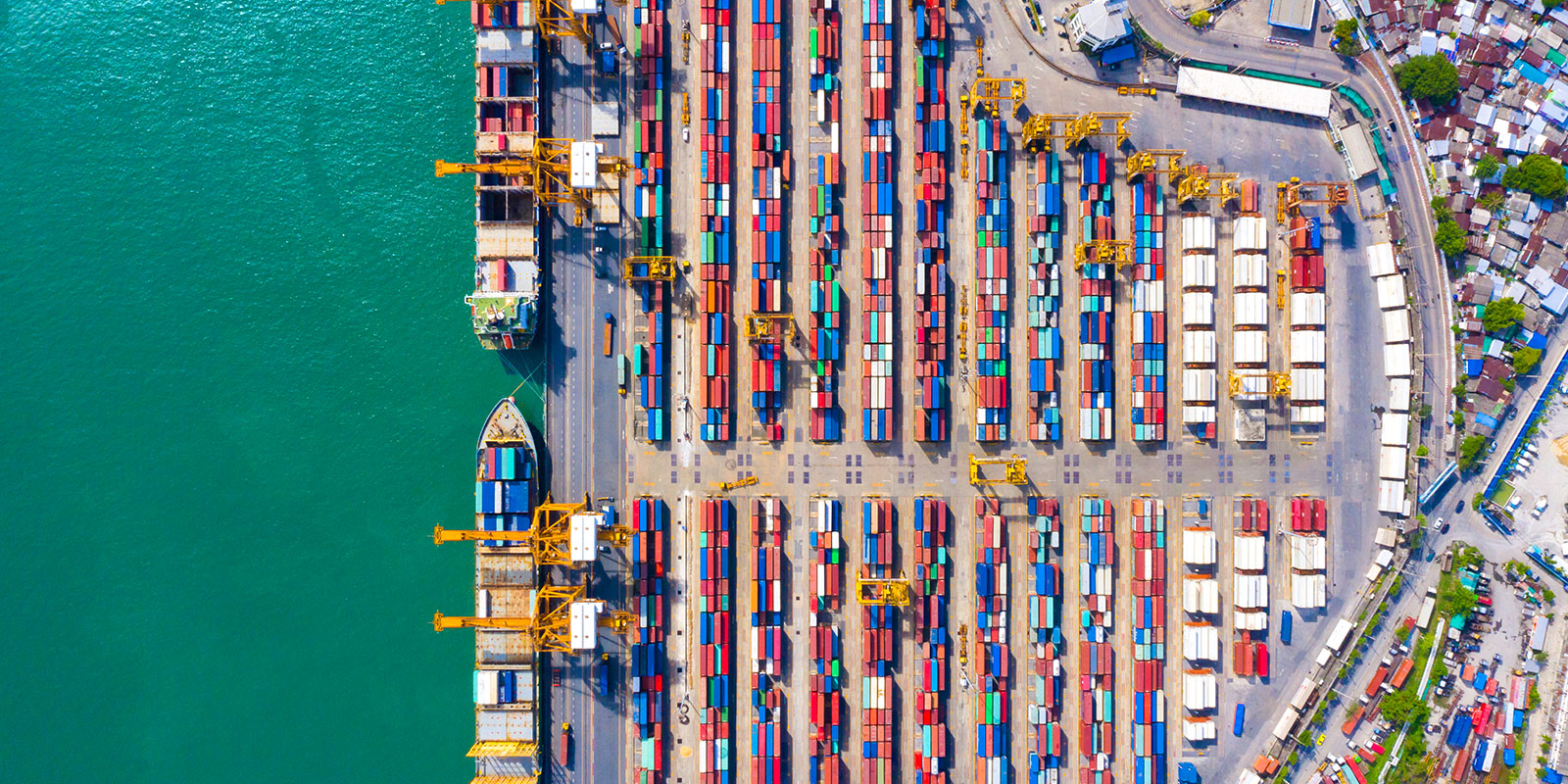 Aerial view of busy shipping port with colourful containers, cranes, and docked ships.