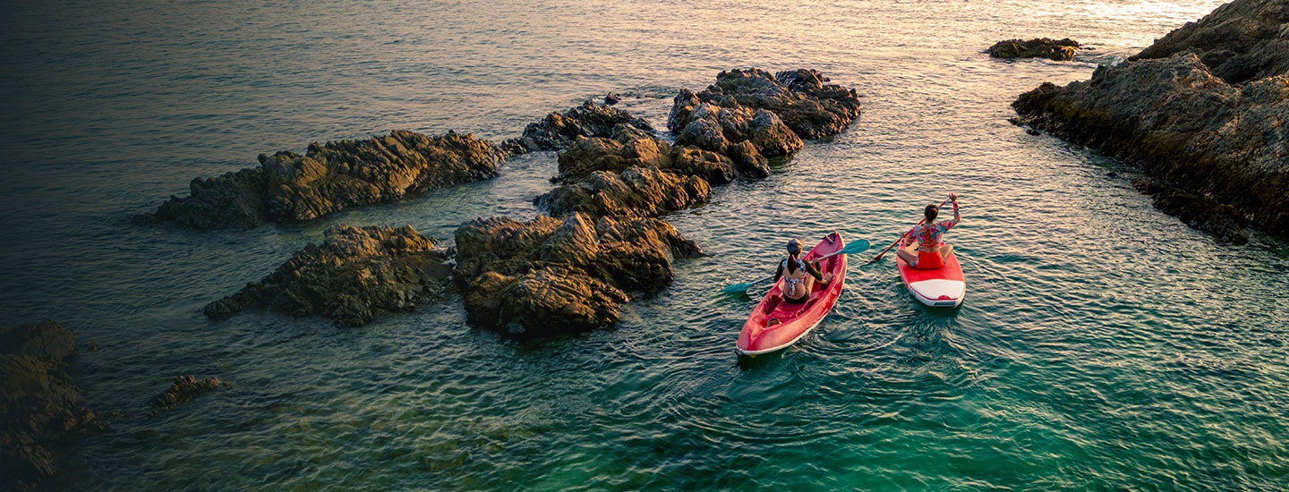 Two people kayaking on clear greenish-blue water, surrounded by rocky formations.
