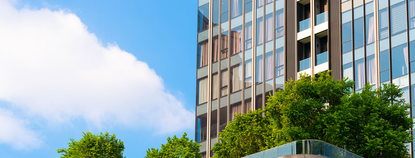 Modern high-rise building with glass windows and balconies, with trees in front.