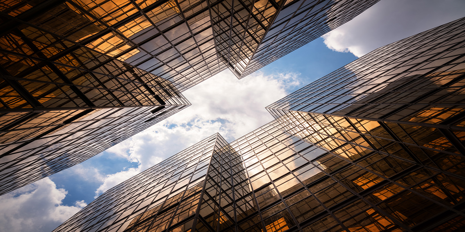 Upward view of tall reflective skyscrapers with glass facades and partly cloudy sky