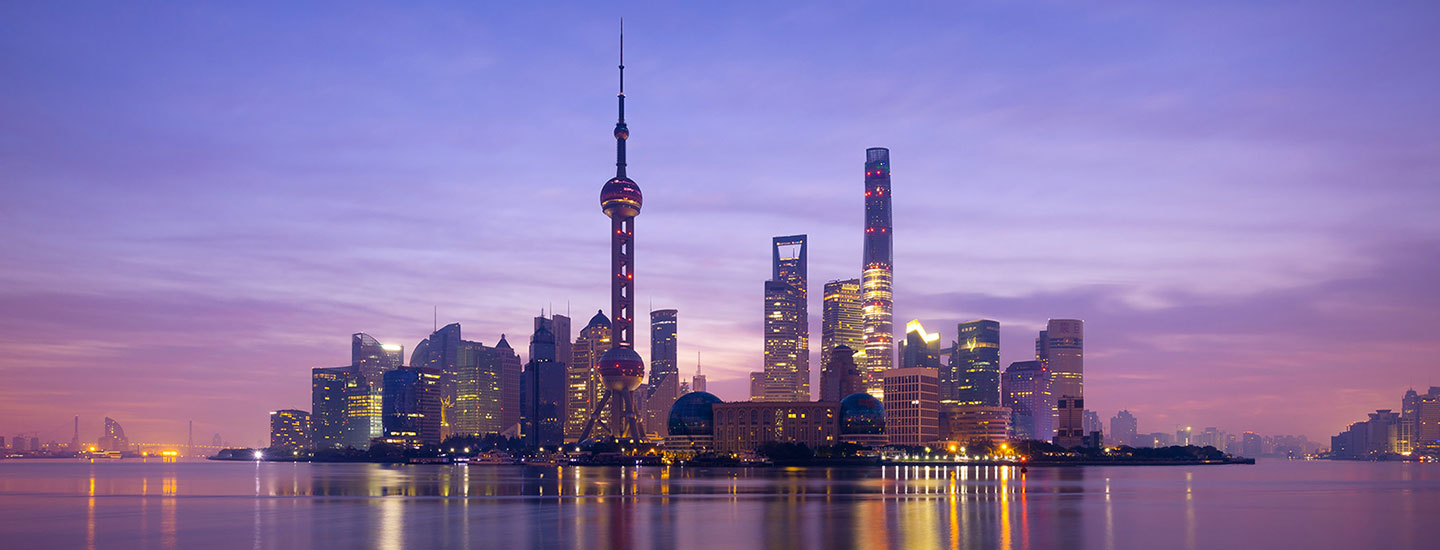 Shanghai skyline at twilight with illuminated skyscrapers, including the Oriental Pearl Tower, reflecting on water.