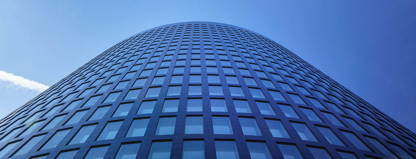 RWE Tower in Dortmund with a curved dark façade, grid-patterned windows, and sloping rooflines under a clear blue sky.